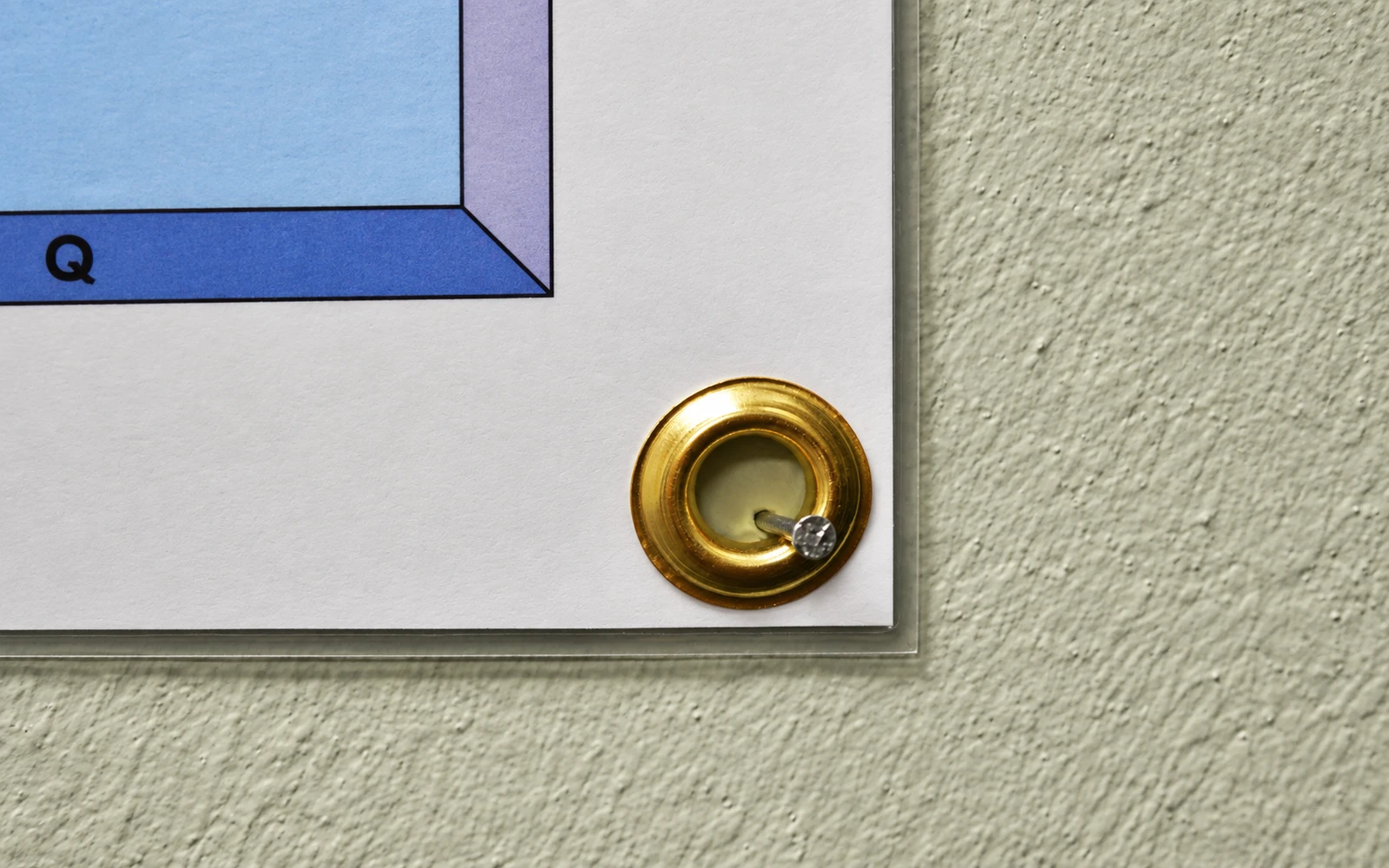 A brass grommet in the corner of a laminated map, fixed to the wall