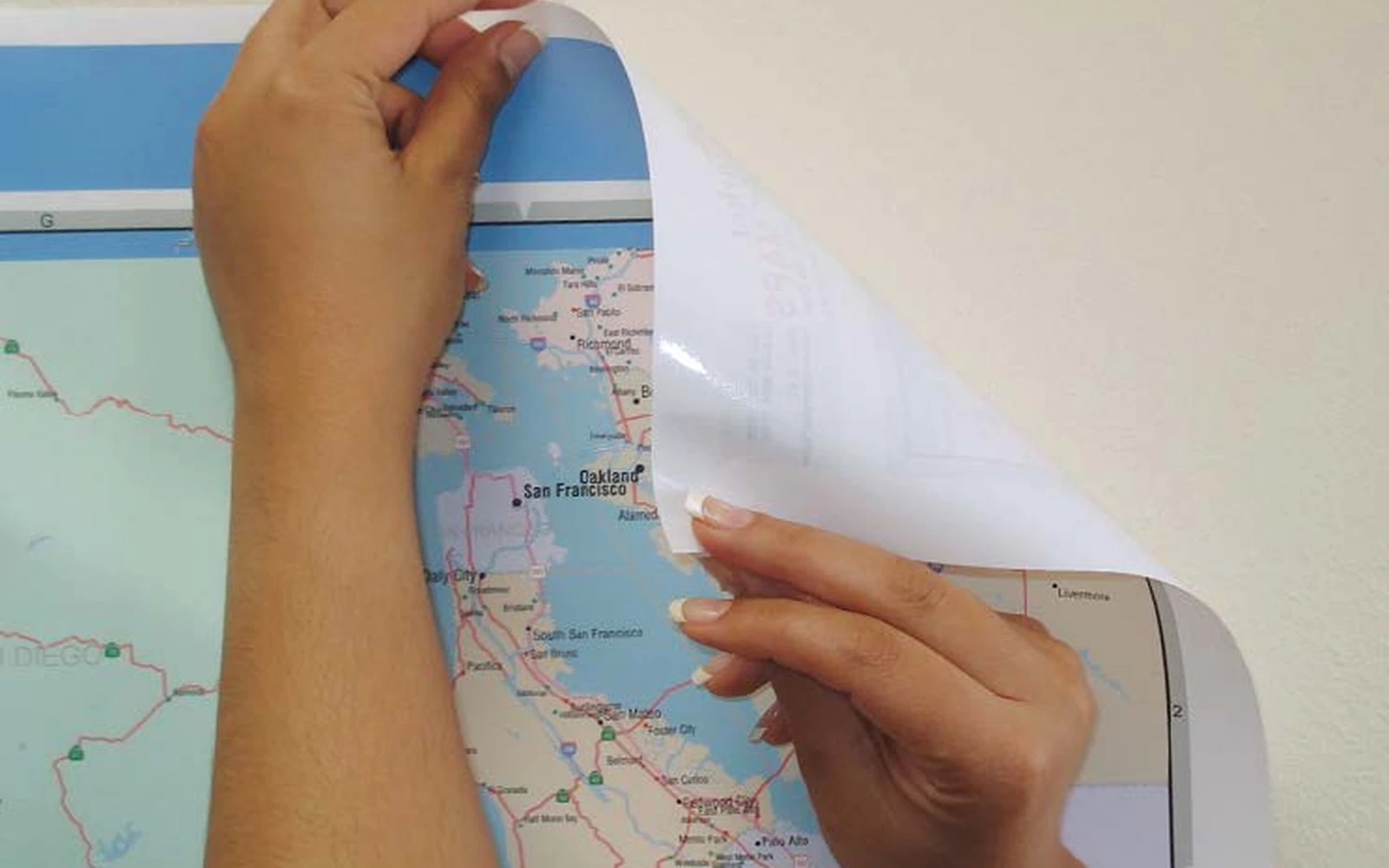Hands peeling a ReSticker map back from a painted wall