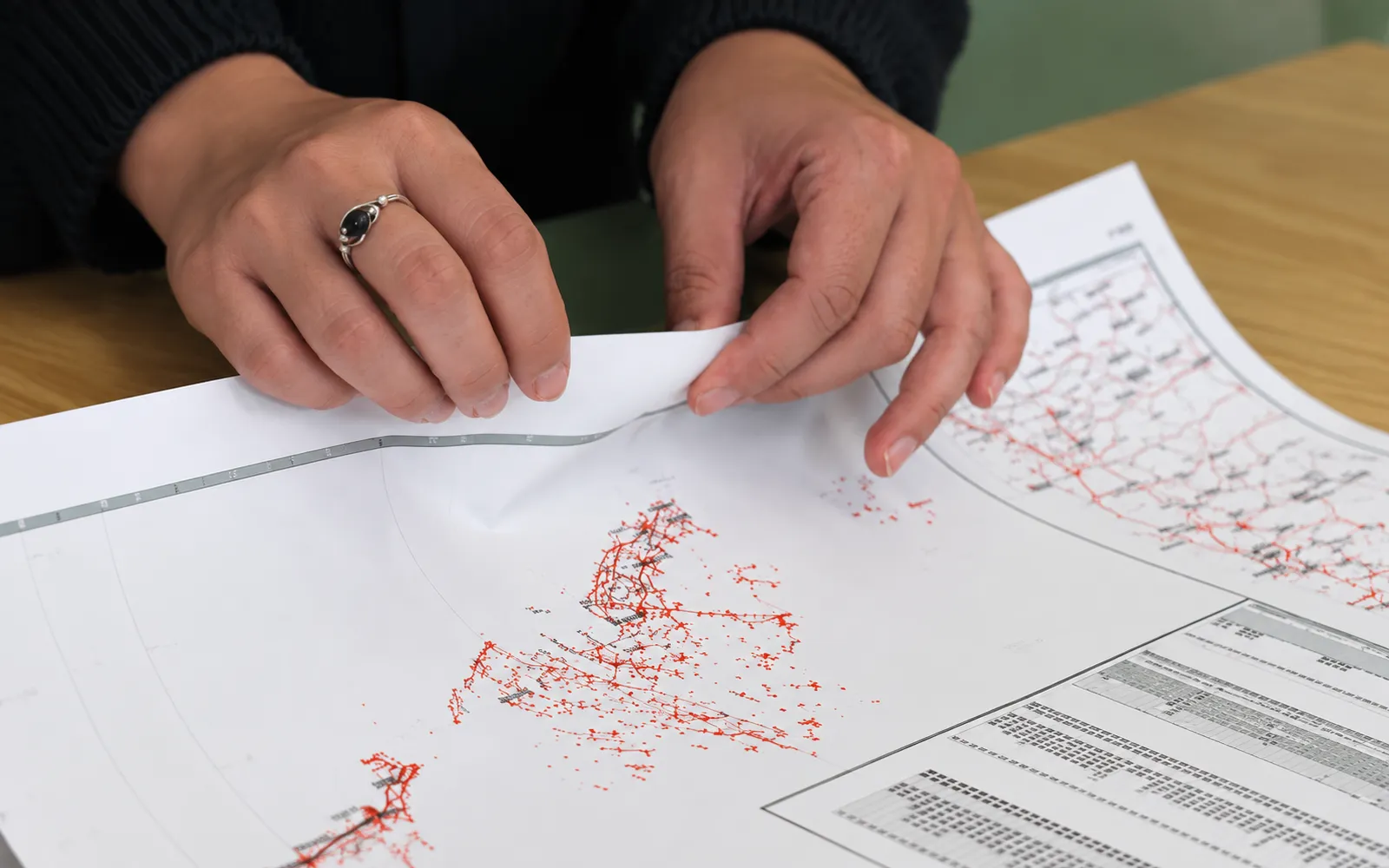 Two hands flexing the edge of a thin, bright-white synthetic map sheet on a desk