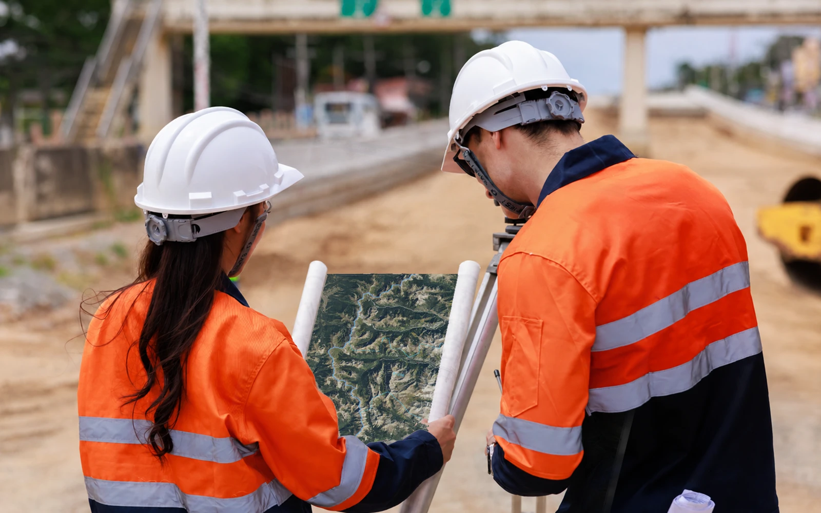 Two site workers in hard hats and high-visibility jackets consulting a map outdoors