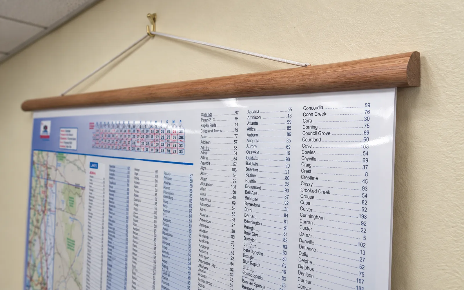 A laminated index map hung from a hardwood rail and cord on a brass wall hook