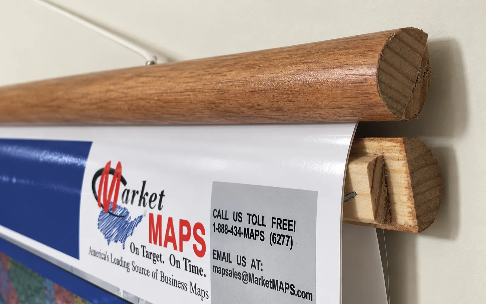 A close-up of a hardwood rail along the top of a laminated map hung by a cord